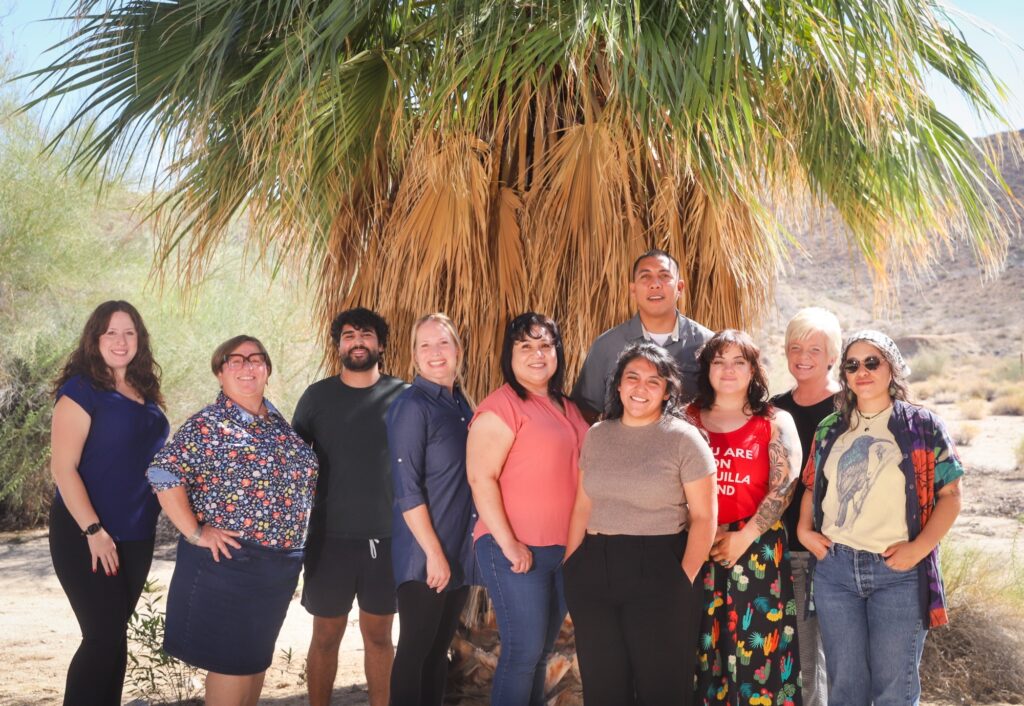 Friends staff of 10 people stadning in front of a California native Fan Palm.